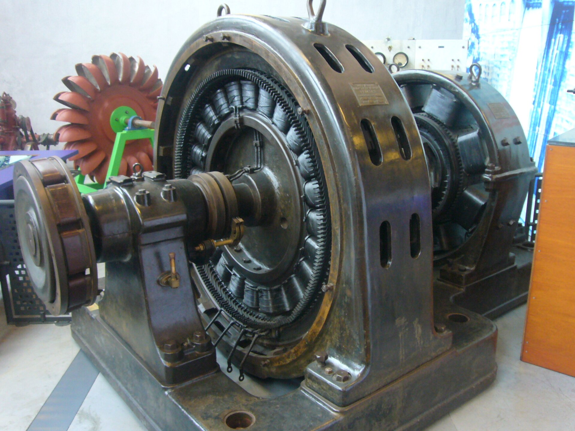 Rys. a. Zdjęcie przedstawia wielkie, skomplikowane urządzenie stojące w hali fabrycznej. Składa się z kilku cylindrów umieszczonych na wspólnej osi. Na obwodzie największego cylindra widać wiele zwojnic, których osie maja kierunek promieni cylindra.