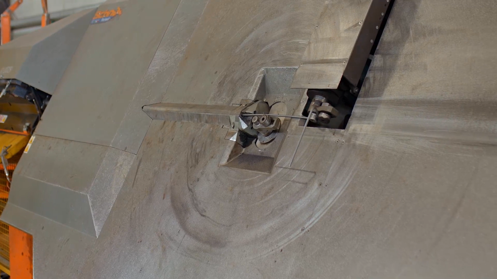 Zdjęcie przedstawia giętarkę mechaniczną o płaskim kształcie, w której środku znajduje się cienki, odginany pręt.