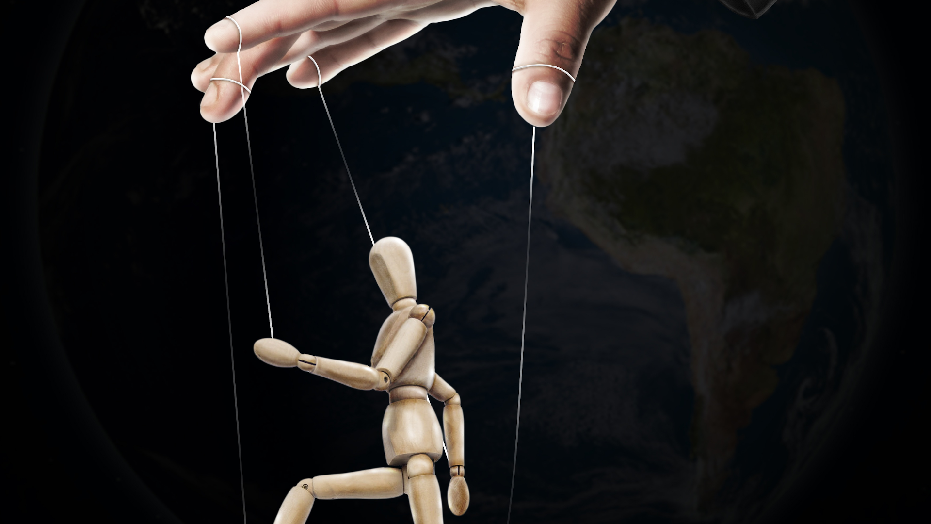 Zdjęcie przedstawia marionetkę. Do drewnianej figurki przyczepione są sznurki. Dłoń człowieka porusza sznurkami. 