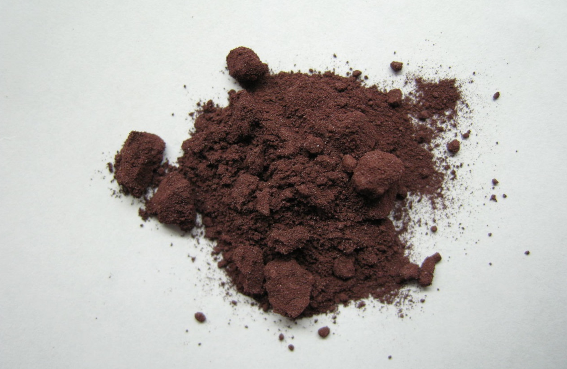 Na ilustracji ukazano stosik ciemnoczerwonego proszku na białej powierzchni.