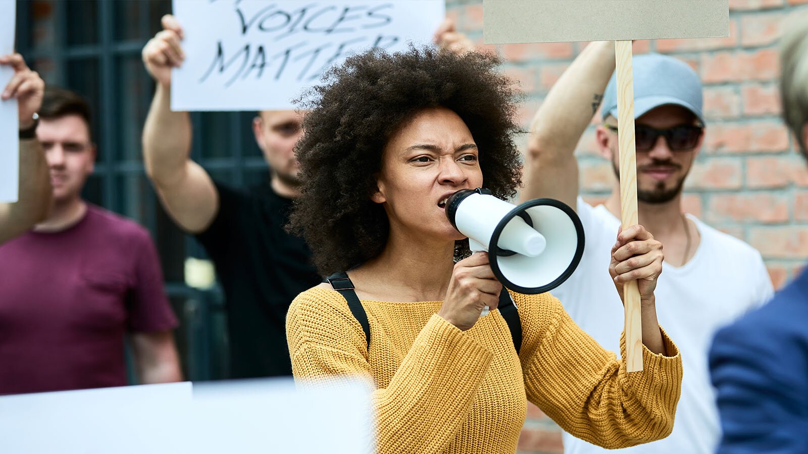 Zdjęcie przedstawia osoby biorące udział w wiecu. Widoczne są transparenty a na centralnym miejscu stoi kobieta z megafonem. 