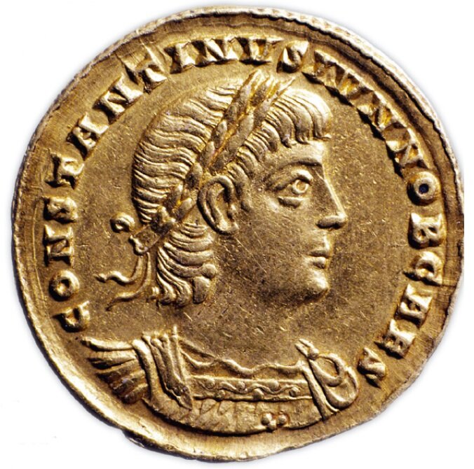 Zdjęcie przedstawia awers antycznej monety. Przedstawia prawy profil mężczyzny. Mężczyzna ma na głowie wieniec laurowy. Wokół niego znajdują się napisy.