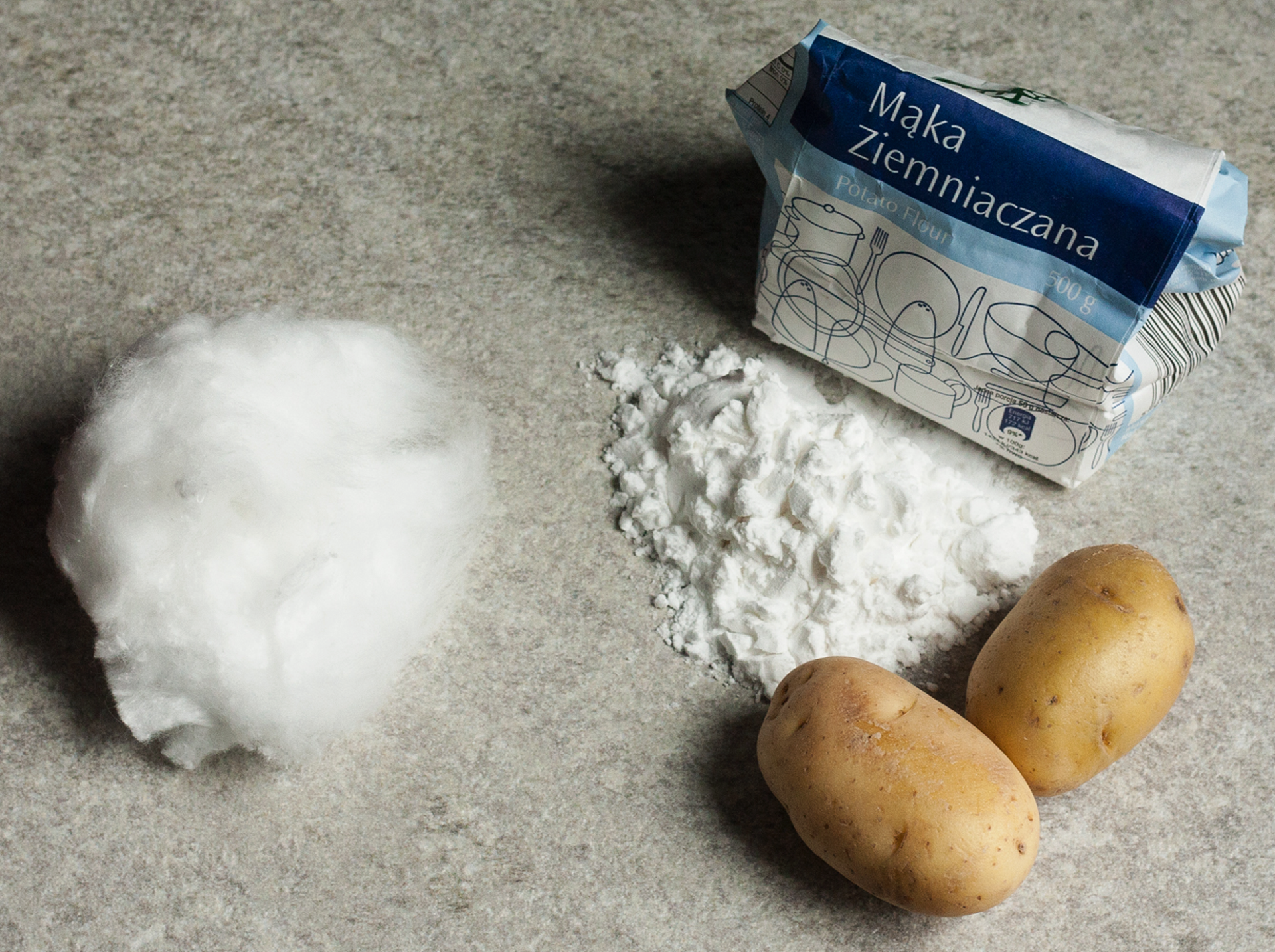 Fotografia przedstawiająca produkty ułożone na stole: mąka ziemniaczana, kartofle, wata celulozowa