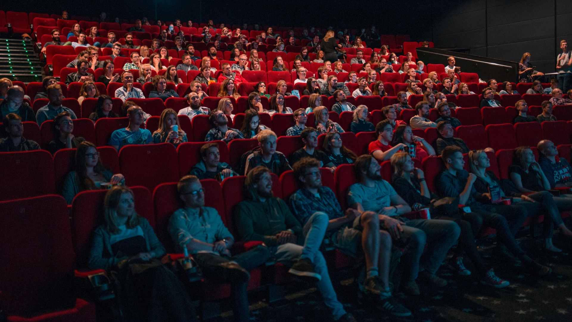 Zdjęcie przedstawia widownie teatralną na parterze. Widownia jest częściowo zapełniona. 