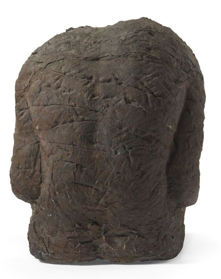 Ilustracja interaktywna. Dzieło Magdaleny Abakanowicz pod tytułem „Plecy” przedstawia figurę odwróconą do widza plecami. Rzeźba jest wykonana z zawiniętych kawałków materiału, tworzących jej kształt i pomalowanych na ciemnobrązowy kolor. Kolory tworzą efekt rdzy. Postać siedzi na podłożu, pozbawiona jest głowy, rąk i nóg. Postać jest zgarbiona i pochylona do dołu. Faktura rzeźby jest chropowata, nierówna, szorstka wynikająca z rodzaju zastosowanego materiału w prototypie odlewu rzeźby  - jutowego płótna.