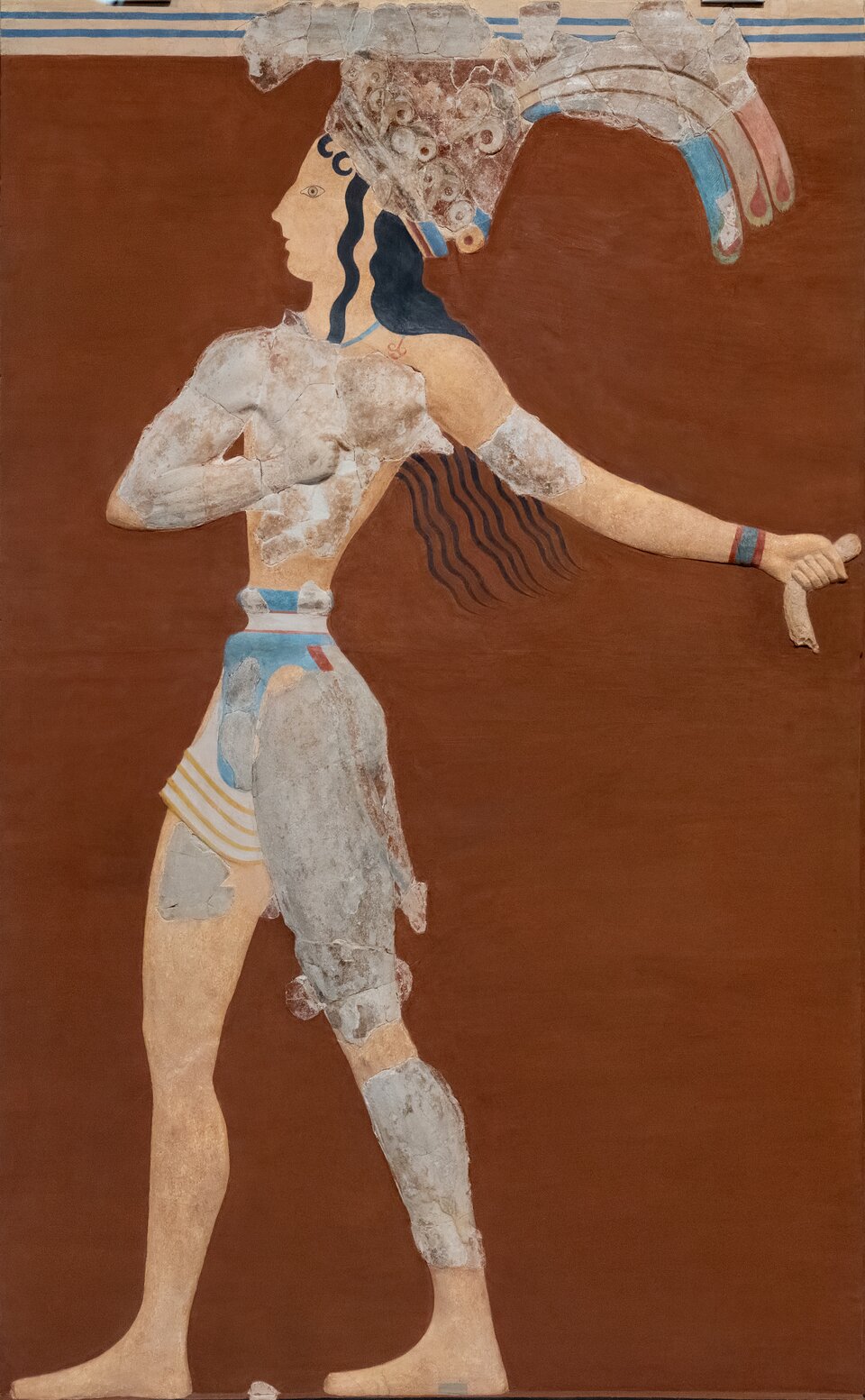 Ilustracja przedstawia kroczącego młodego mężczyznę ukazanego na czerwonym tle. Mężczyzna wykonuje krok do przodu, a jej tors jest wygięty. Naturalnej wielkości postać ma na sobie kolorową przepaskę biodrową, pas oraz majestatyczne nakrycie głowy — koronę z lilii i pawich piór. Włosy mężczyzny są ciemne, długie i falowane, ułożone starannie wokół twarzy. Prawa ręka, zaciśnięta w pięść, przylega do klatki piersiowej. Lewa została wyciągnięta za siebie.