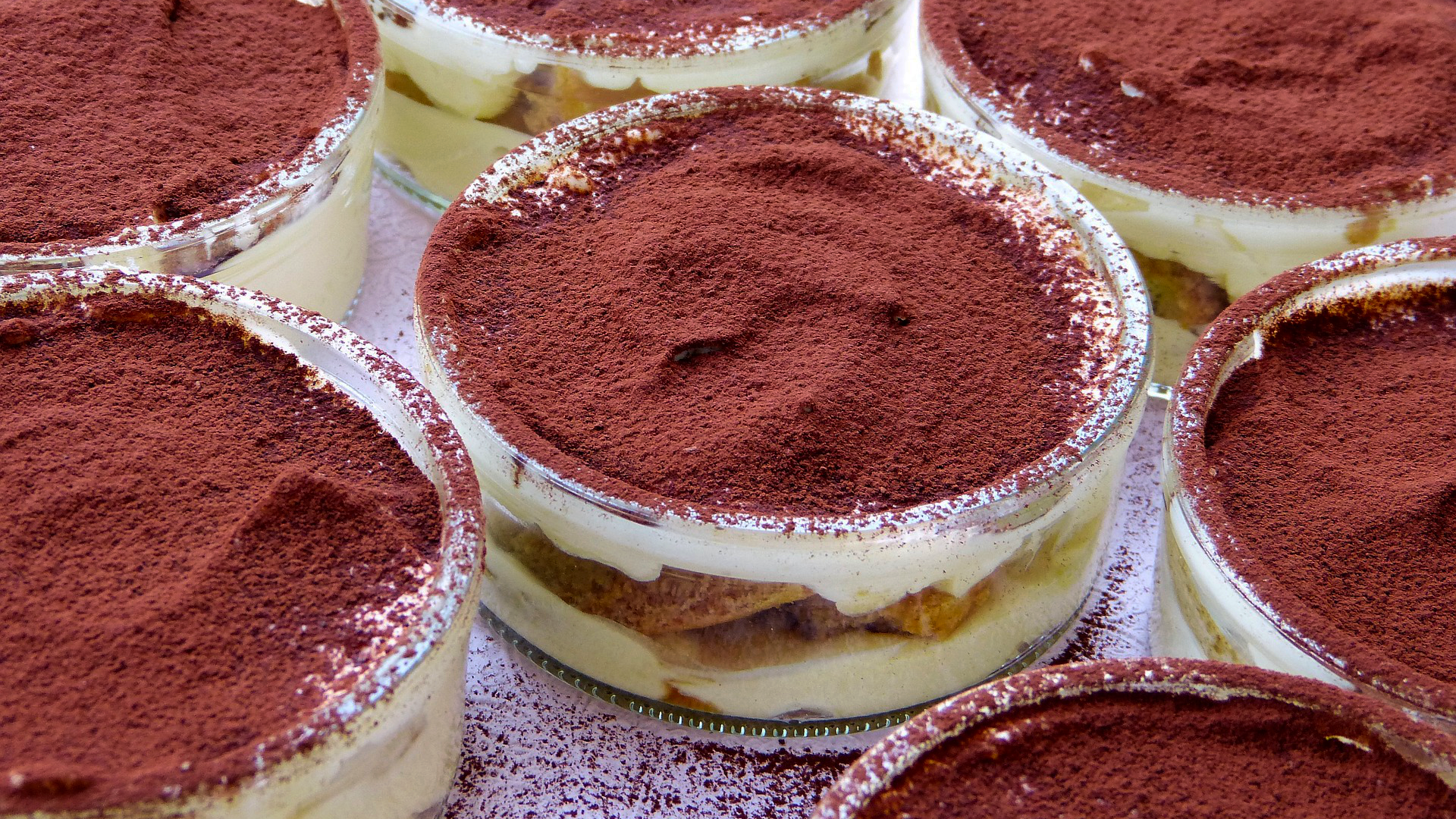 Zdjęcie przedstawia kilka deserów tiramisu w szklanych salaterkach.