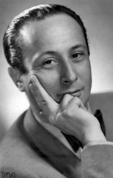 Ilustracja przedstawia czarno‑białą fotografię dojrzałego mężczyzny. Jego wzrok skierowany jest w stronę widza. Jego oczy są ciemne, nos prosty, czoło wysokie. Jego włosy są ciemne, zaczesane do tyłu. Prawą ręką mężczyzna podpiera głowę. Mężczyzna ubrany jest w jasną marynarkę, czarną muszkę pod szyją i białą koszulę.