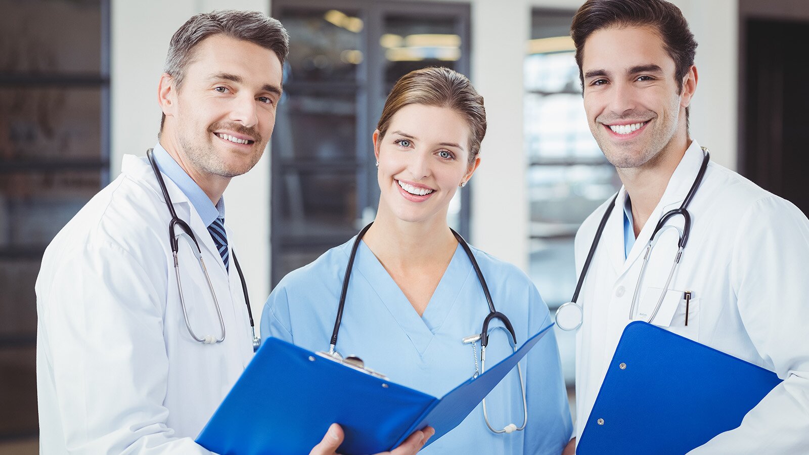 Zdjęcie przedstawia troje młodych ludzi w fartuchach lekarskich i zawieszonymi na szyję stetoskopami. 