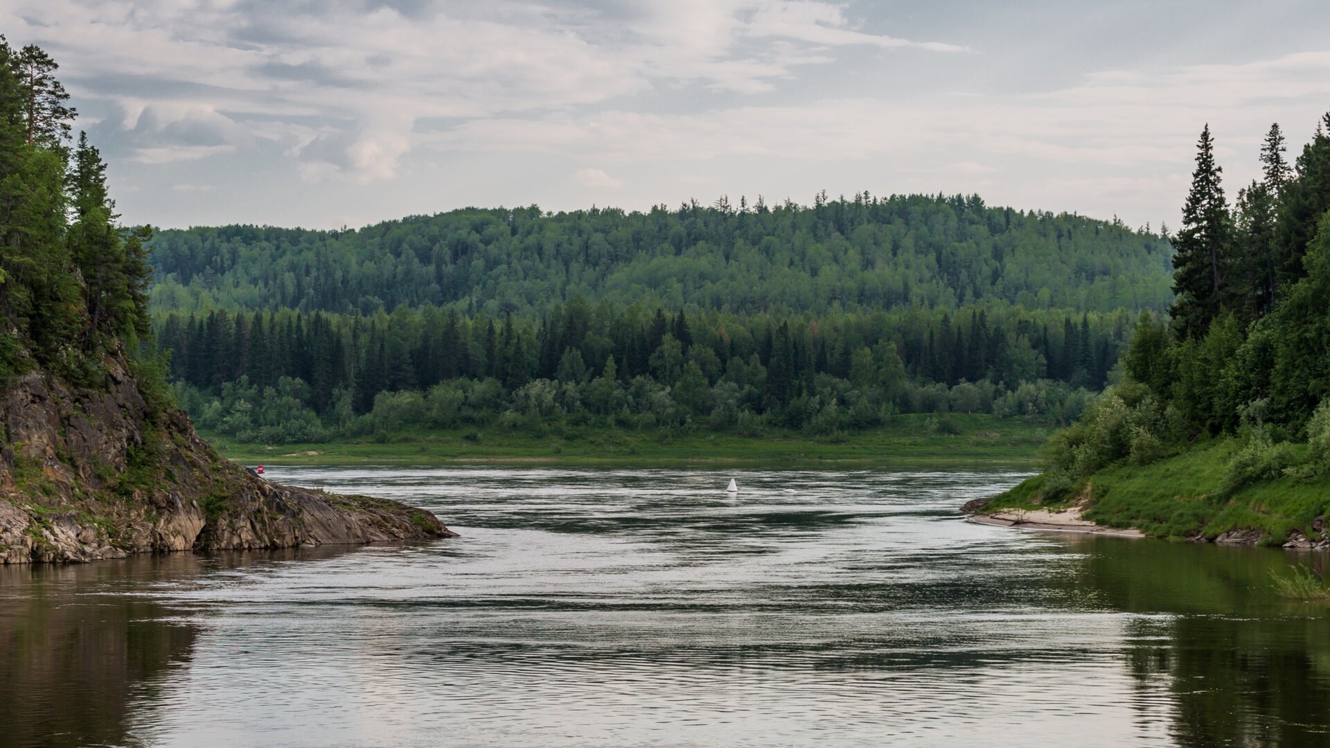Fotografia przedstawiająca krajobraz nad rzeką Jenisej w środkowej Syberii w azjatyckiej części Rosji. Na pierwszym planie przewężenie rzeki. Po obu stronach spadziste brzegi z drzewami iglastymi. W tle wzgórze porośnięte lasem iglastym.
