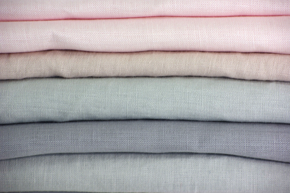Zdjęcie przedstawia ułożone jeden na drugim, zwinięte materiały w delikatnych odcieniach różu, beżu i szarości.