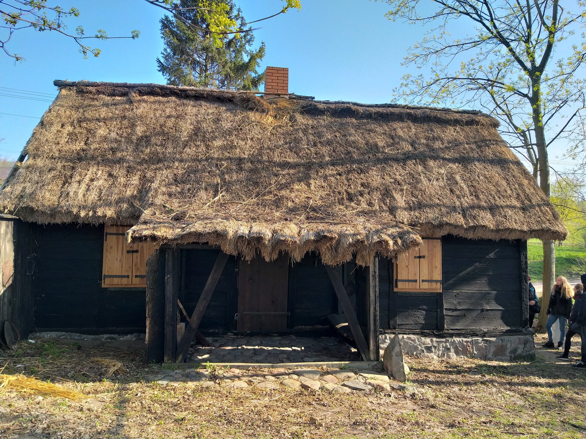 Fotografia przedstawia drewnianą chatę ze słomianym dachem. Kamienny fundament, zamknięte drewniane okiennice.