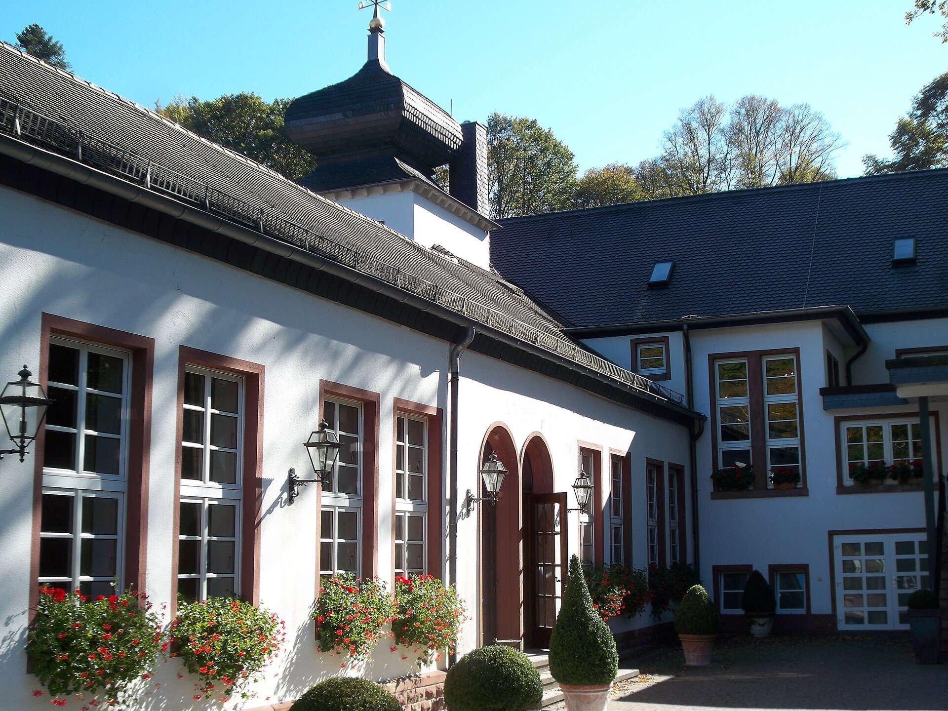 Widoczny fragment rezydencji Tschifflik w Zweibrücken w Palatynacie. Kompleks budynków tzw. Bażantarii zbudowanych w stylu mołdawskim. Widać przylegające do budynku głównego skrzydło boczne. Parterowy dom mieszkalny, skierowany na dziedziniec ogrodowy. W oknach widać skrzynki z pnącymi kwiatami i stojące donice z iglakami. Dachy budynków pokryte są ciemną dachówką