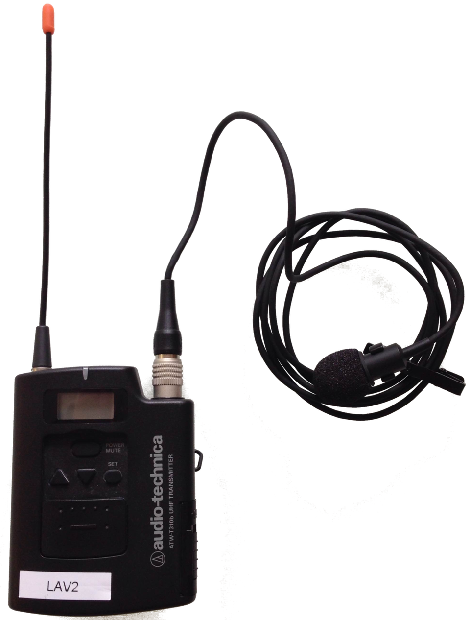 Zdjęcie przedstawia bezprzewodowy mikrofon z nadajnikiem. Niewielkie, prostokątne urządzenie, w górnej części posiada krótką antenkę, a obok gniazdo do którego podłączony jest długi kabel z niewielkim mikrofonem. Mikrofon ten można przypiąć do ubrania za pomocą zapinki.