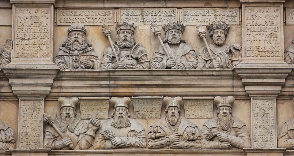 Ilustracja przedstawia płaskorzeźbę ścienną. Widocznych jest osiem postaci, prawdopodobnie królów. Obok każdego znajdują się tablice z wybitymi w kamieniu napisami.