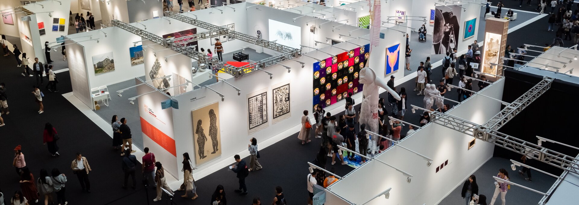 W wielkim pomieszczeniu znajduje się wiele białych ścian. Powieszone są na nich obrazy o różnej wielkości i kolorystyce. Nad każdym dziełem wisi biała lampa. Dookoła ścian znajduje się tłum ludzi, który stoi na szarej podłodze.   