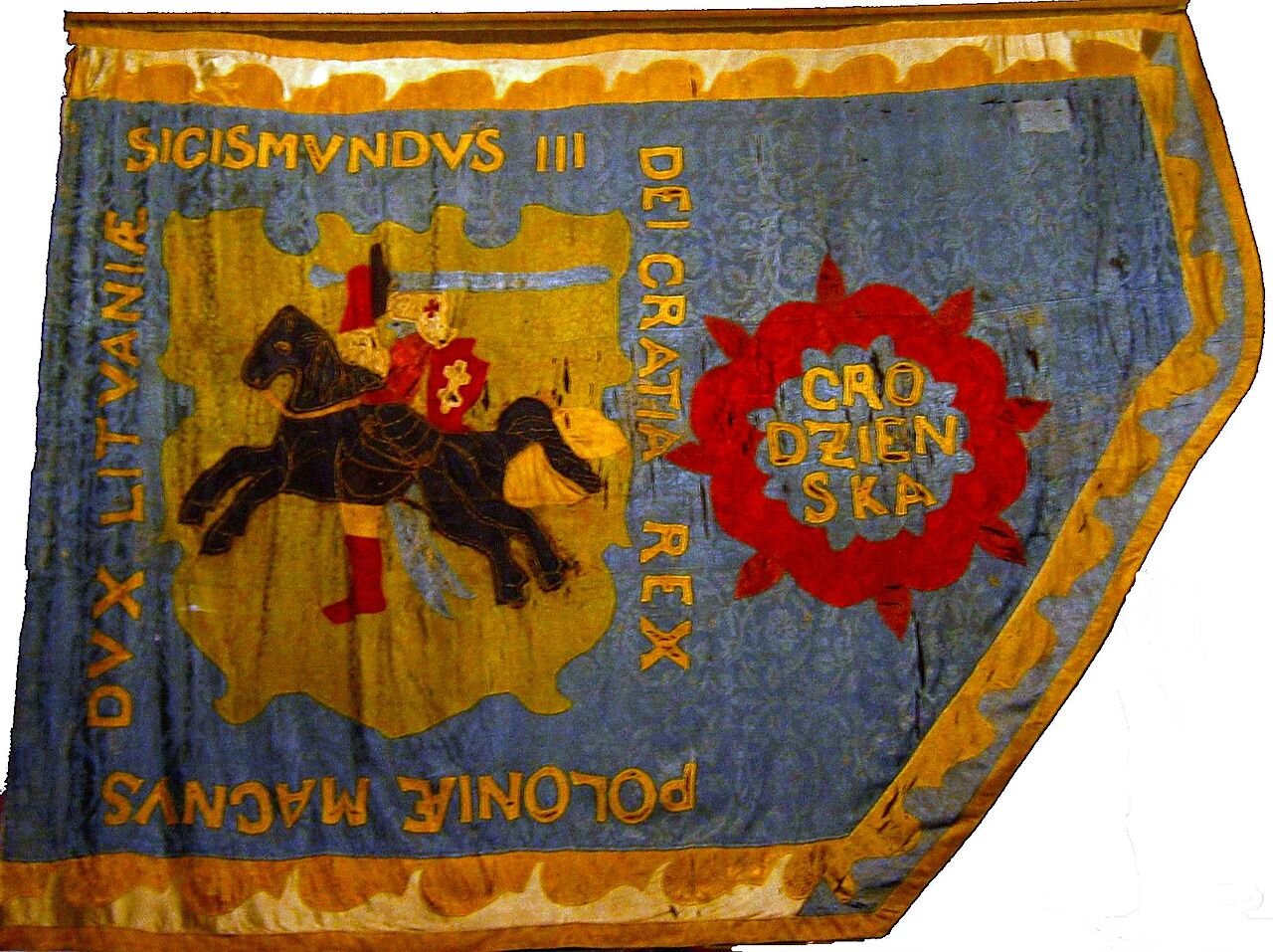 Zdjęcie ukazuje fragment chorągwi pospolitego ruszenia powiatu grodzieńskiego z 1619 roku. Na chorągwi jest mężczyzna z mieczem siedzący na koniu. Wokół niego znajduje się napis po łacinie. 
