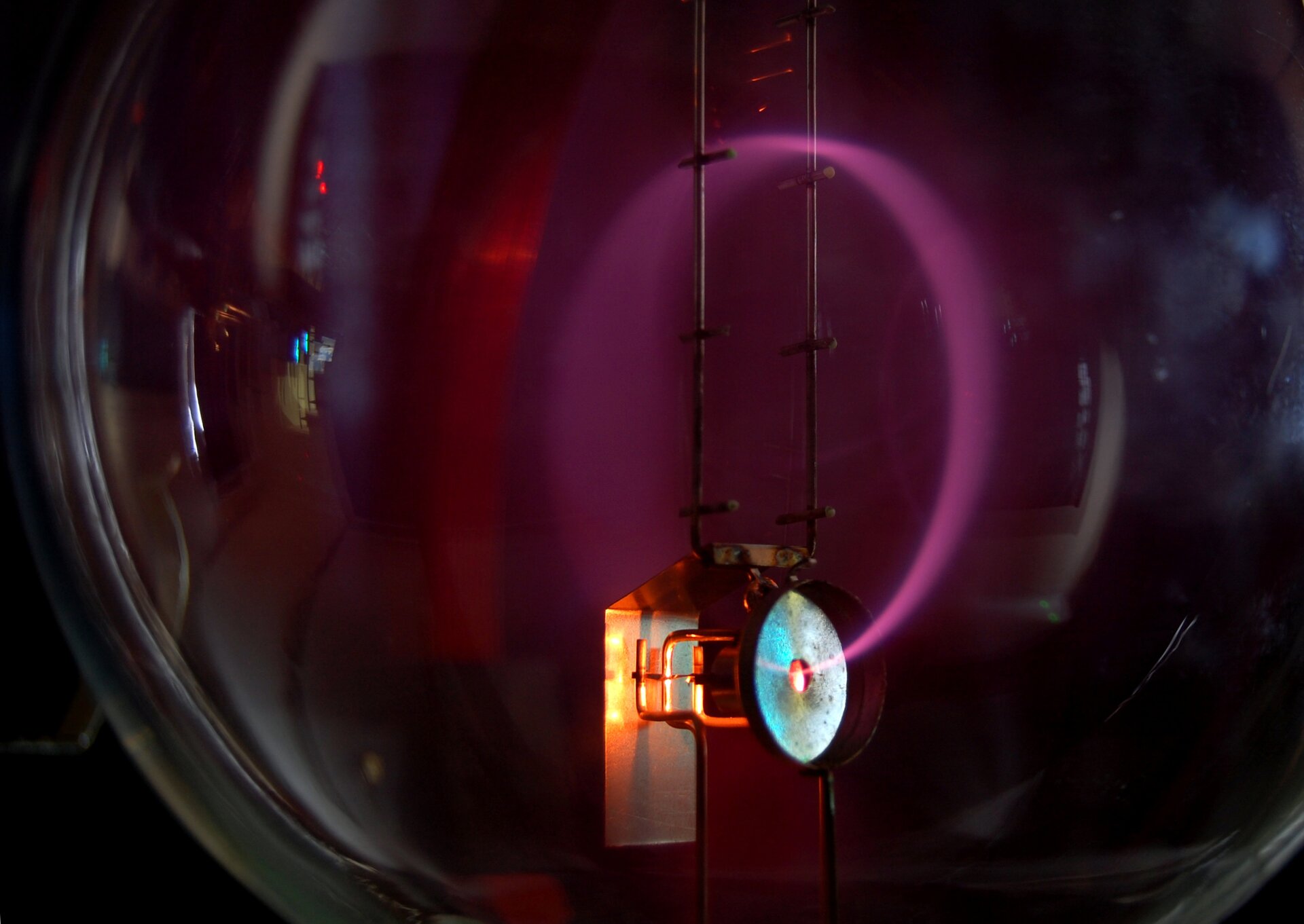 Rys. 2. Na zdjęciu widać wnętrze szklanej kuli, w której znajduje się małe jasne kółeczko, z którego emitowana jest wiązka elektronów. Tor ruchu elektronów to świecący fioletowo kolisty pas o rozmytych brzegach. 