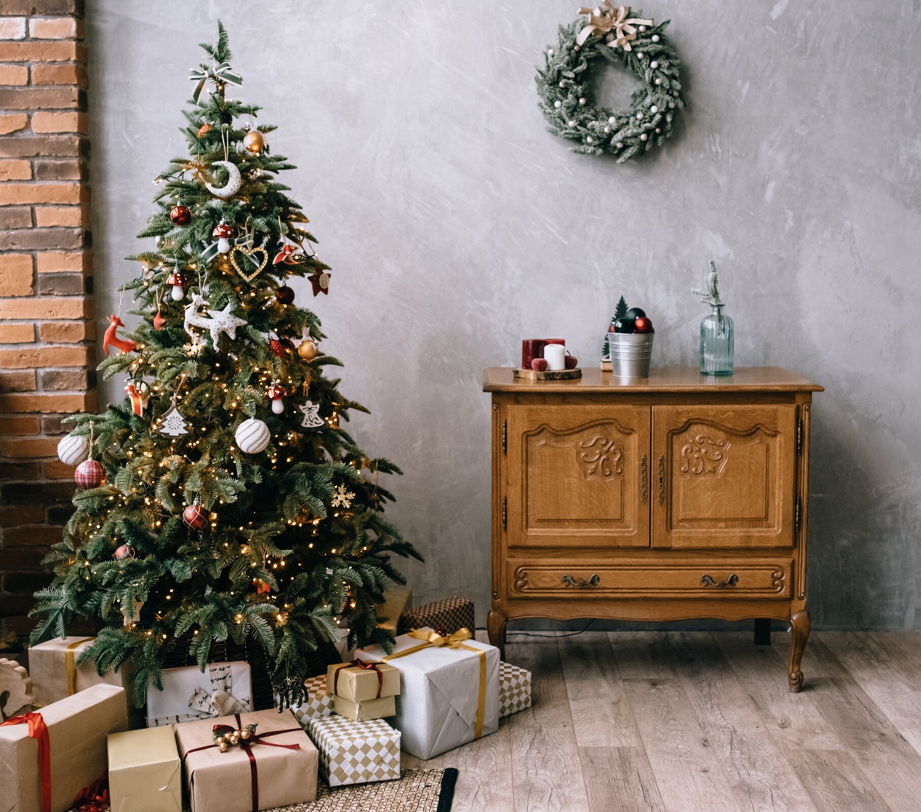 Ilustracja ukazuje wnętrze pokoju, w którym stoi pięknie udekorowana choinka. Pod drzewkiem  znajdują się opakowane prezenty. 