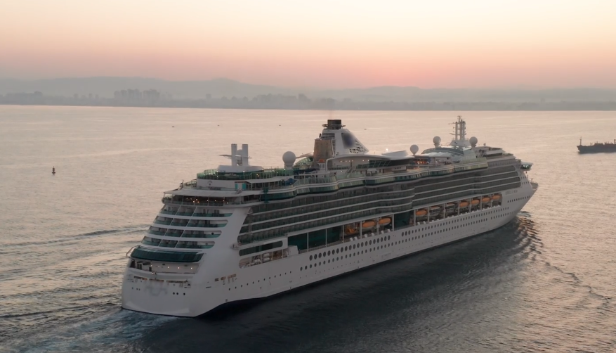 Zdjęcie przedstawia statek pasażerski. Posiada on koło z łopatami na boku oraz pojedynczy komin na środku. W tle widać góry.