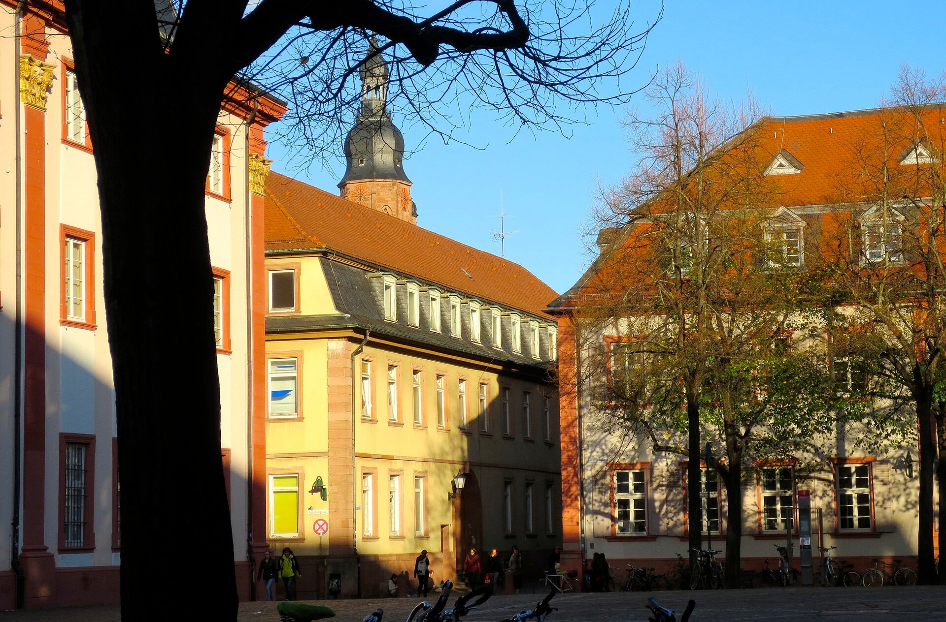 Zdjęcie przedstawia niewielki plac, przy którym usytuowane są trzy duże budynki. Jeden z nich zwieńczony jest niewielką wieżyczką.