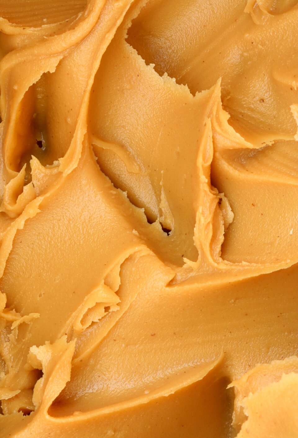 Na grafice ukazano zbliżenie n masło orzechowe. Jest ono koloru pomarańczowo–brązowego, z widocznymi śladami pozostawionymi przez nóż.