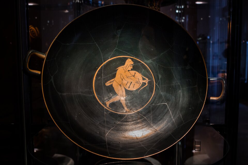 Ilustracja przedstawia fragment naczynia czerwonofigurowego.  W centralnej części wnętrza przedstawiony jest wojownik z łukiem. Postać ta ukazana jest w dynamicznej pozie – nosi tradycyjną scytyjską czapkę. Łucznik wyposażony jest w nagolenniki, tarczę, kołczan oraz łuk,.