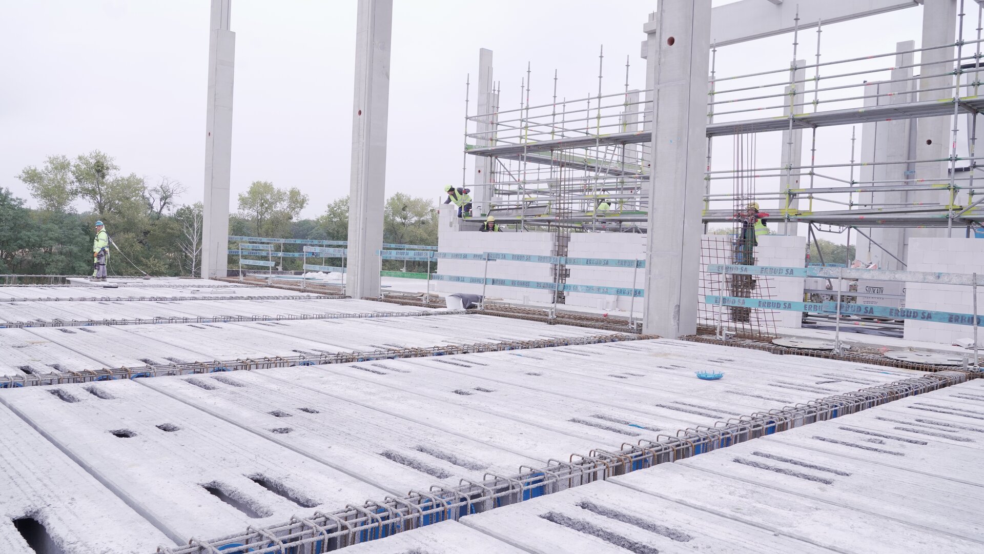 Zdjęcie przedstawia zbrojenie stropu. W tle widać robotników pracujących przy malowej konstrukcji.