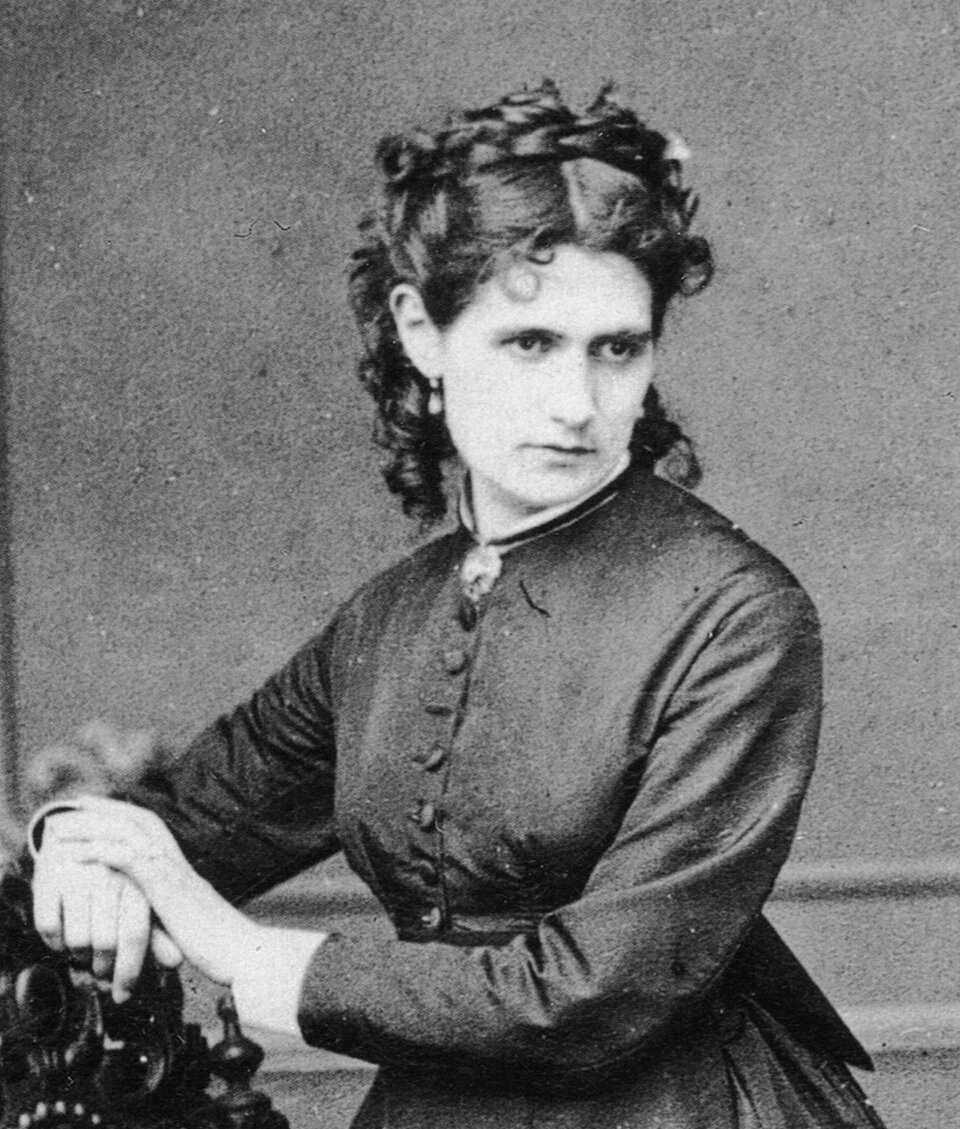 Ilustracja przedstawia malarkę Berthę Morisot.
Kobieta siedzi i pozuje do zdjęcia. Ubrana jest w czarną suknię. Włosy ma kręcone, upięte do tyłu. dłonie opiera na poręczy krzesła. Postać kobiety ukazana jest do pasa, jej twarz zwrócona jest w kierunku widza.