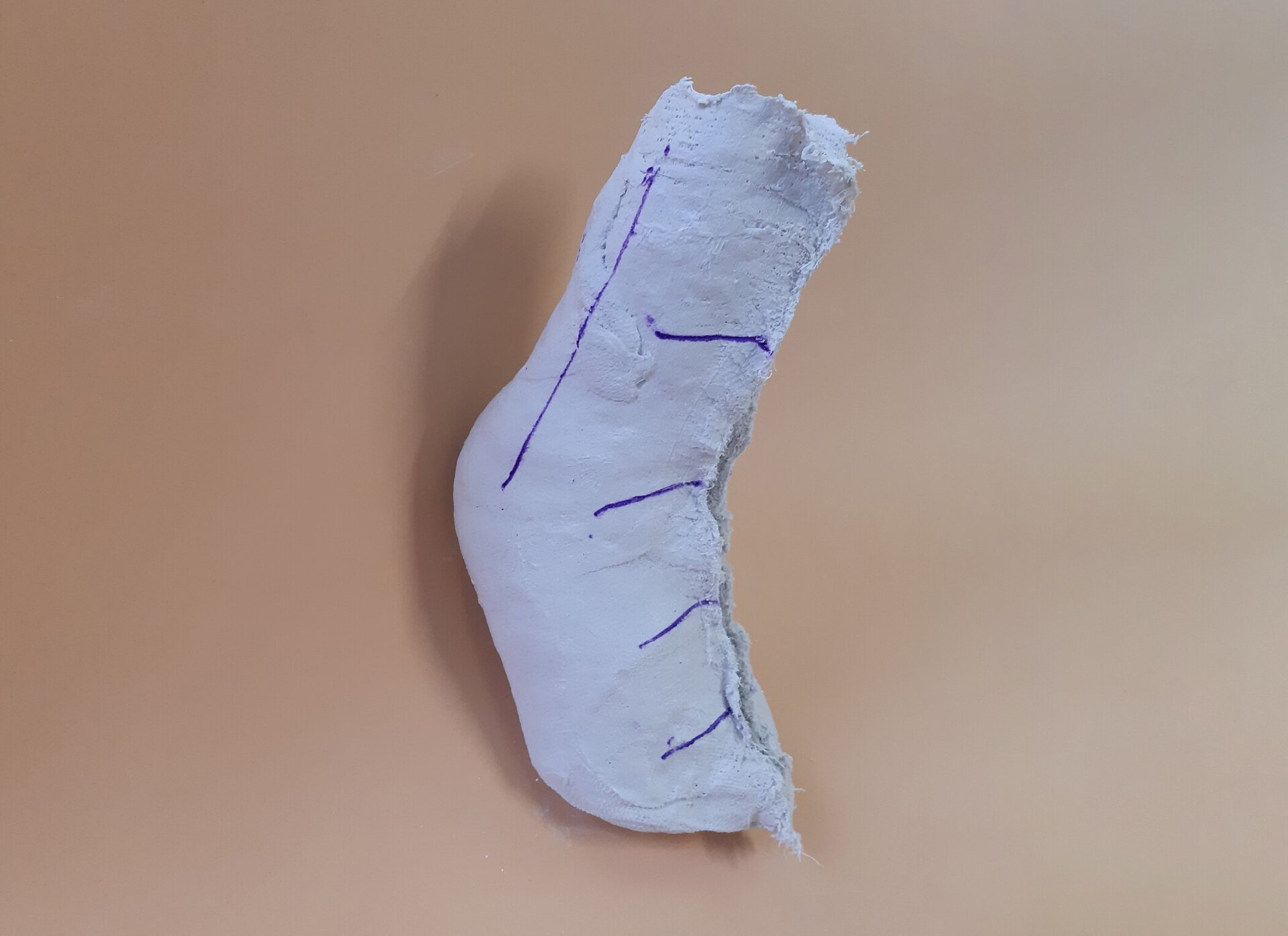 Zdjęcie pod tytułem: Negatyw gipsowy. Zdjęcie przedstawia mającą kształt stopy formę gipsową, na której zaznaczone są linie wzdłuż rejonu kostki i grzbietu. 