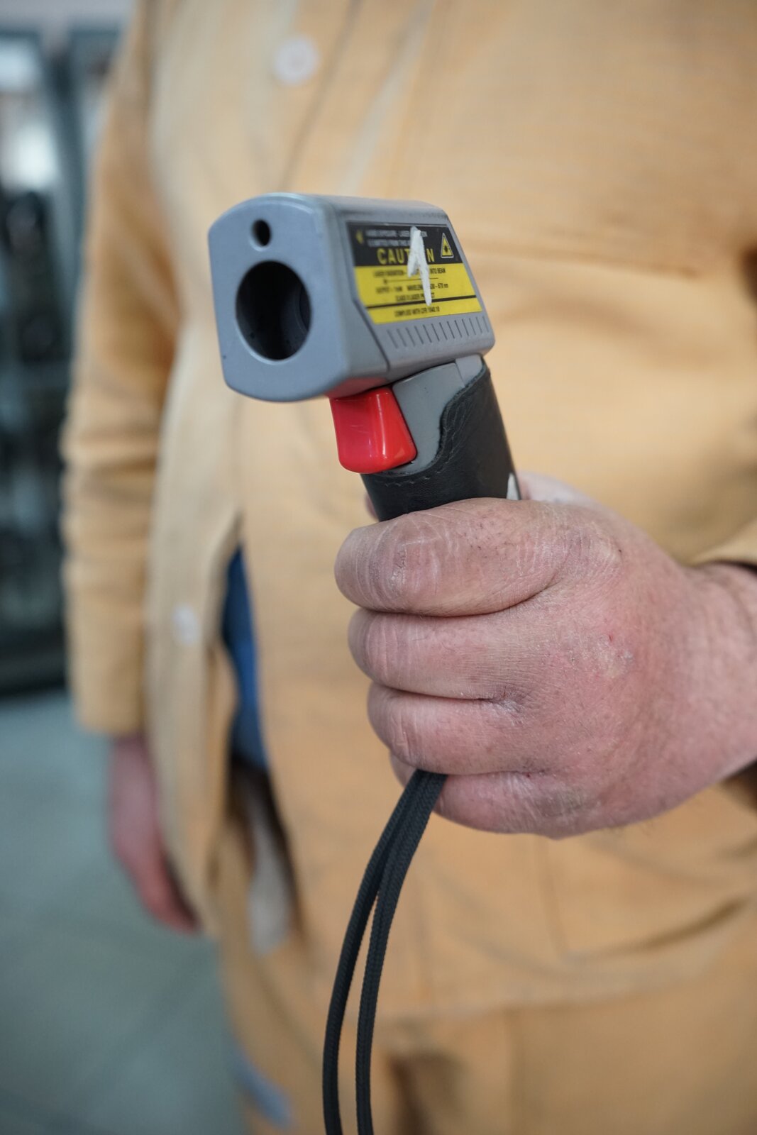 Zdjęcie przedstawia pirometr trzymany w dłoni przez górnika. Jest on ubrany w strój ochronny. Urządzenie wyposażone jest w uchwyt pistoletowy. Na nim osadzona jest nieduża prostopadłościenna część odpowiadająca za pomiar. Na przedniej ścianie znajduje się otwór, którym do wnętrza pirometru trafia promieniowanie cieplne. Pozwala to na bezdotykowy pomiar temperatury. Nad rękojeścią wbudowany jest czerwony przycisk, przypominający spust.