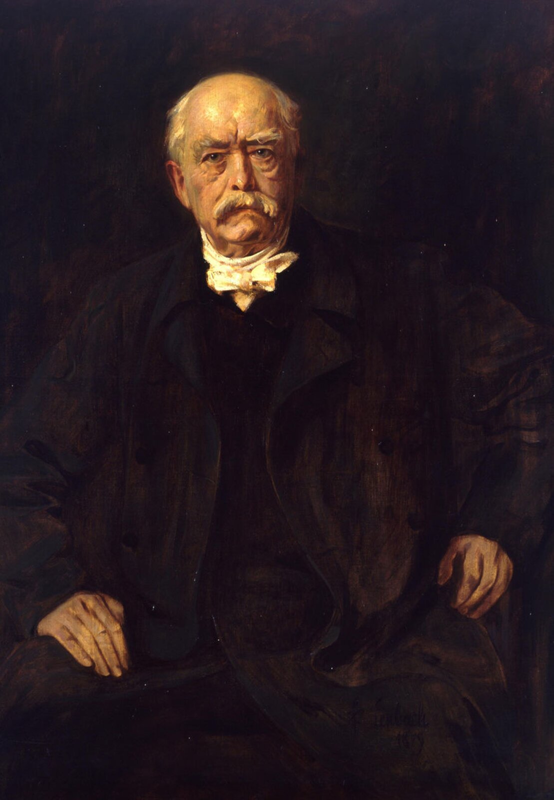 Obraz przedstawiający portret Otto von Bismarcka. Jest to stary mężczyzna, łysy po bokach nad uszami ma kępki siwych włosów, duże krzaczaste siwe brwi oraz siwe długie wąsy. Ubrany jest w czarną szatę, pod szyją ma wywiązaną białą chusteczkę. Siedzi na krześle na udach opiera dłonie.