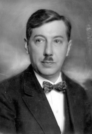 Zdjęcie przedstawia mężczyznę w średnim wieku. Mężczyzna ma krótkie, gładkie, zaczesane na prawą stronę włosy. Jego twarz jest owalna, a nos duży. Mężczyzna ma niewielki wąs pod samym nosem. Mężczyzna ubrany jest w smoking z muszką.