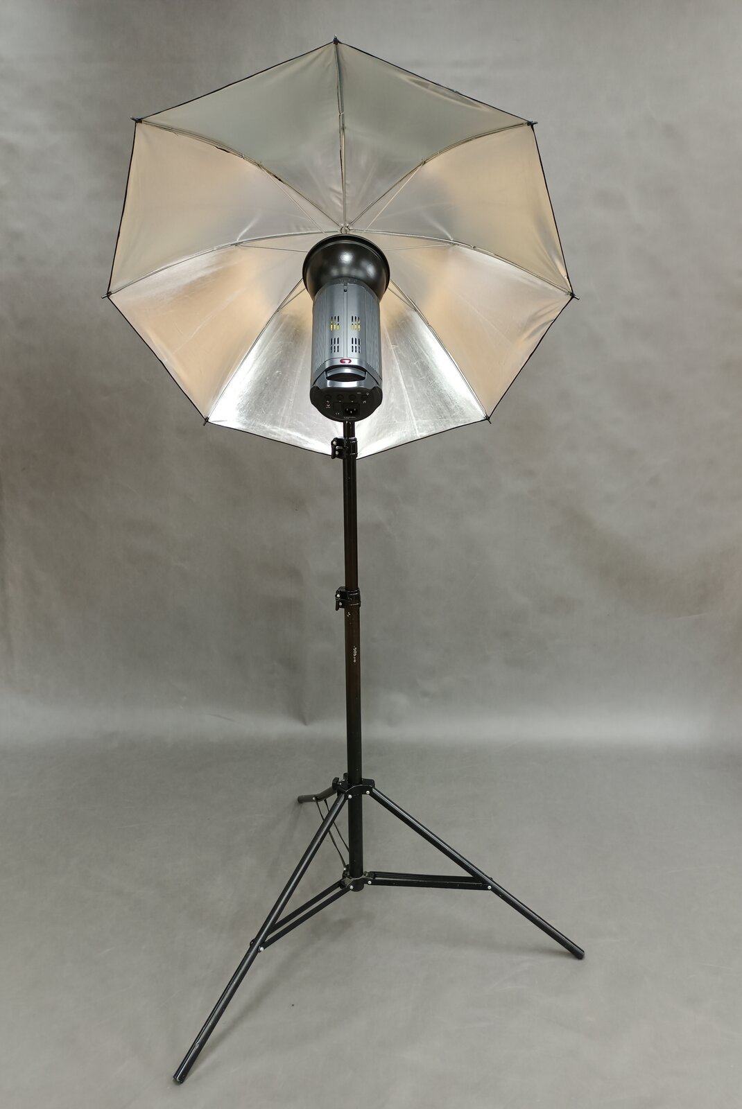 Zdjęcie przedstawia przykładowy statyw z rozstawionymi trzema nogami oraz głowicą znajdującą się w jego górnej części, do której mocuje się lampy oświetleniowe lub też lampy i dyfuzor.