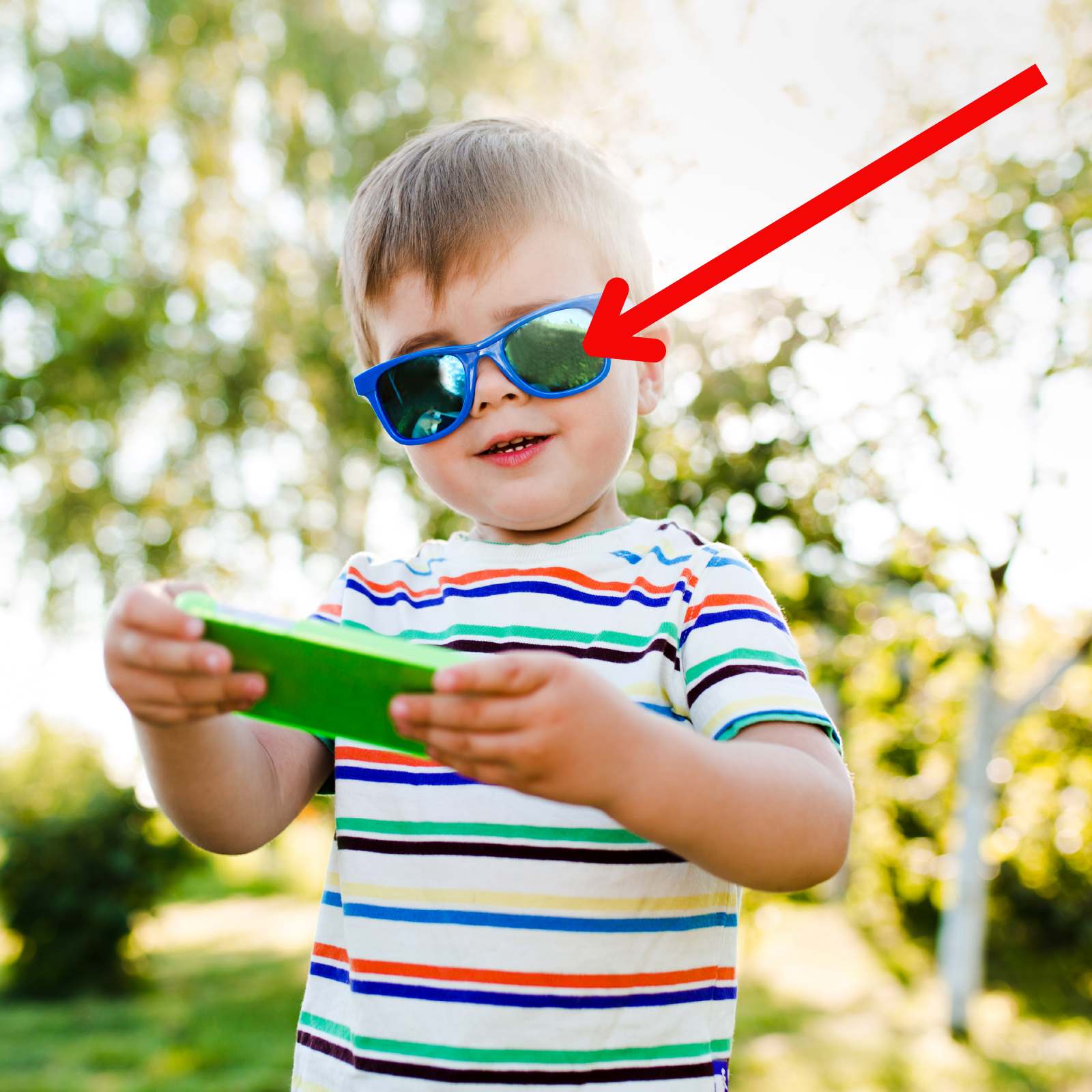Zdjęcie przedstawia małego chłopca trzymającego telefon. Czerwona strzałka wskazuje jego okulary przeciwsłoneczne.