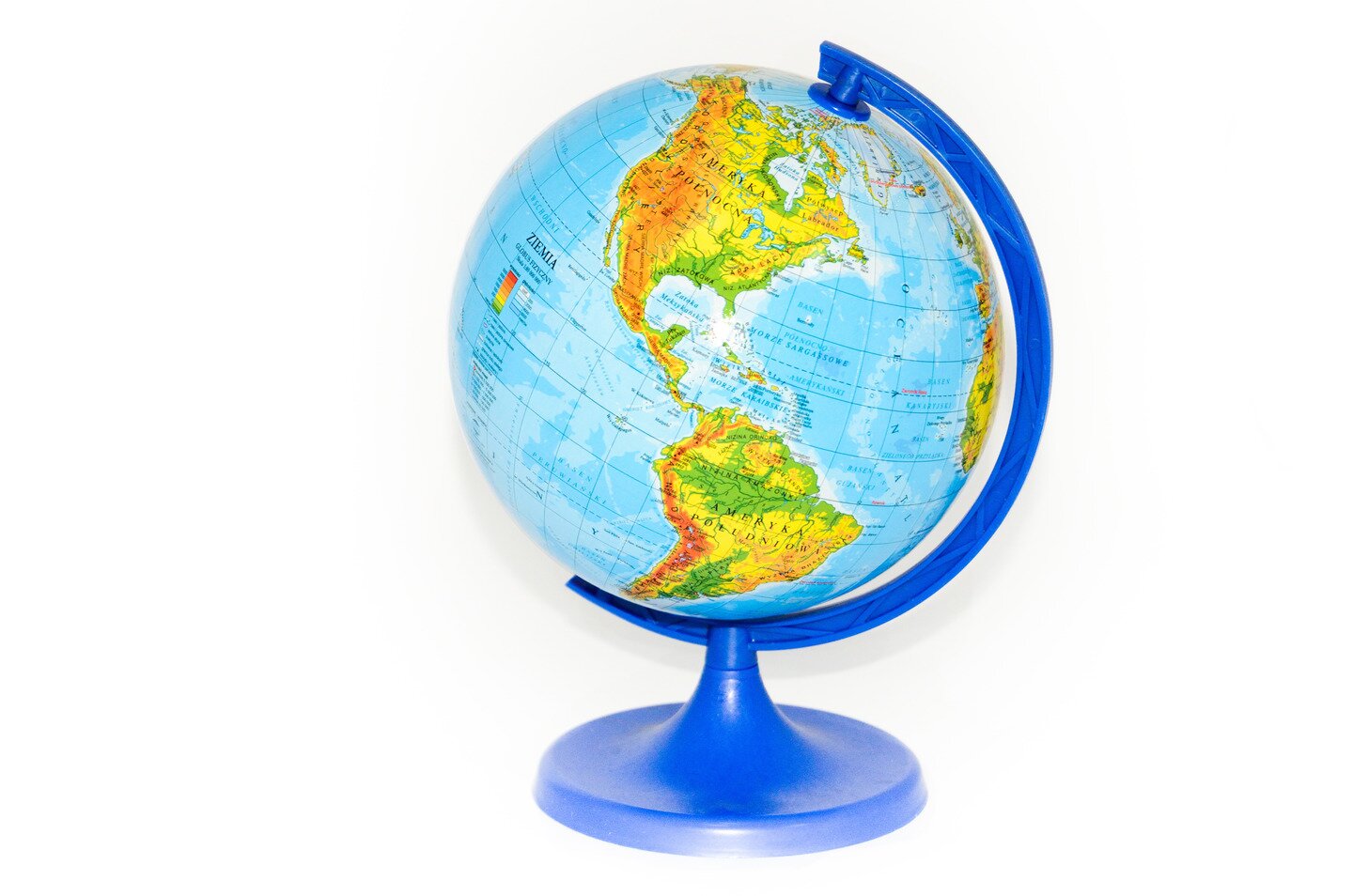 Fotografia prezentuje model Ziemi – globus. Na powierzchni globusa widoczne żółto- brązowo-zielone kontynenty otoczone niebieskimi wodami. Globus stoi na niebieskiej podstawce.