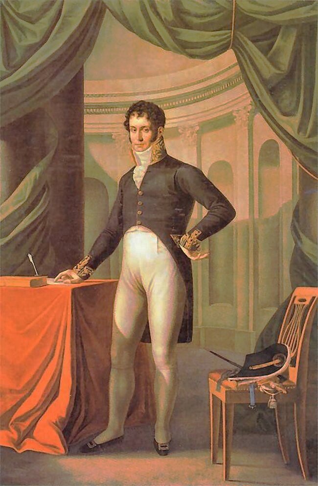 Obraz przedstawia portret mężczyzny. Stoi przy stoliku z czerwonym suknem. Mężczyzna po pociągłą twarz z ciemnymi, kręconymi włosami. Ubrany jest w mundur z ciemną górą i białymi spodniami. Ma wysoki kołnierz i białą apaszkę. Prawą rękę opiera na stoliku, a lewą na biodrze. Za mężczyzną widoczne są kolumny oraz zielona kotara.