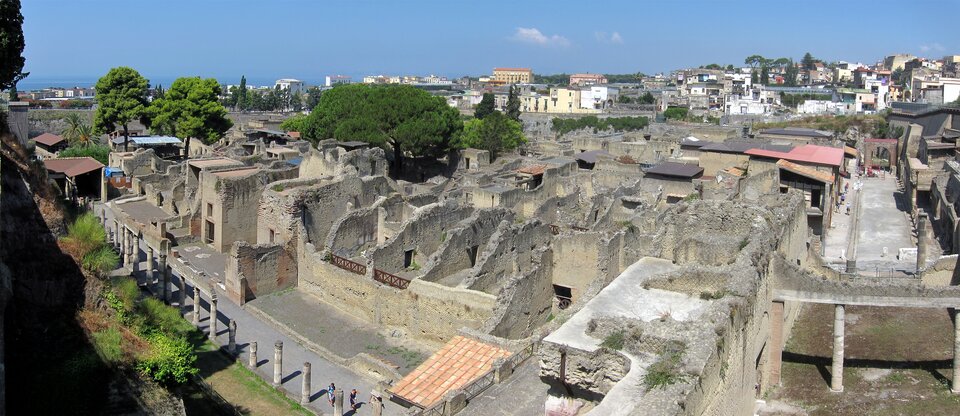 Ilustracja o kształcie poziomego prostokąta  przedstawia widok z góry na Herkulanum. Zaprezentowany został widok od strony Wezuwiusza. Zdjęcie prezentuje ruiny starożytnego miasta z widoczną w tle współczesną zabudową oraz krajobrazem naturalnym. 