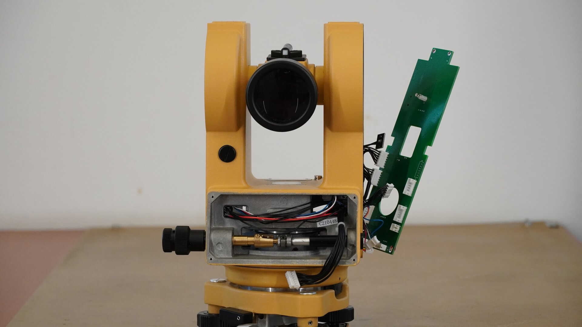 Zdjęcie ukazuje ujęcie instrumentu pomiarowego od strony obiektywu. Pod obiektywem znajduje się miejsce, w którym był zamontowany wyświetlacz. Po jego demontażu widoczne są cienkie przewody zespołów zasilających oraz mechanizm sterowany pokrętłem śruby leniwej. Za nimi widoczne jest koło podziałowe poziome odpowiedzialne za odczyt kąta ruchu poziomego.