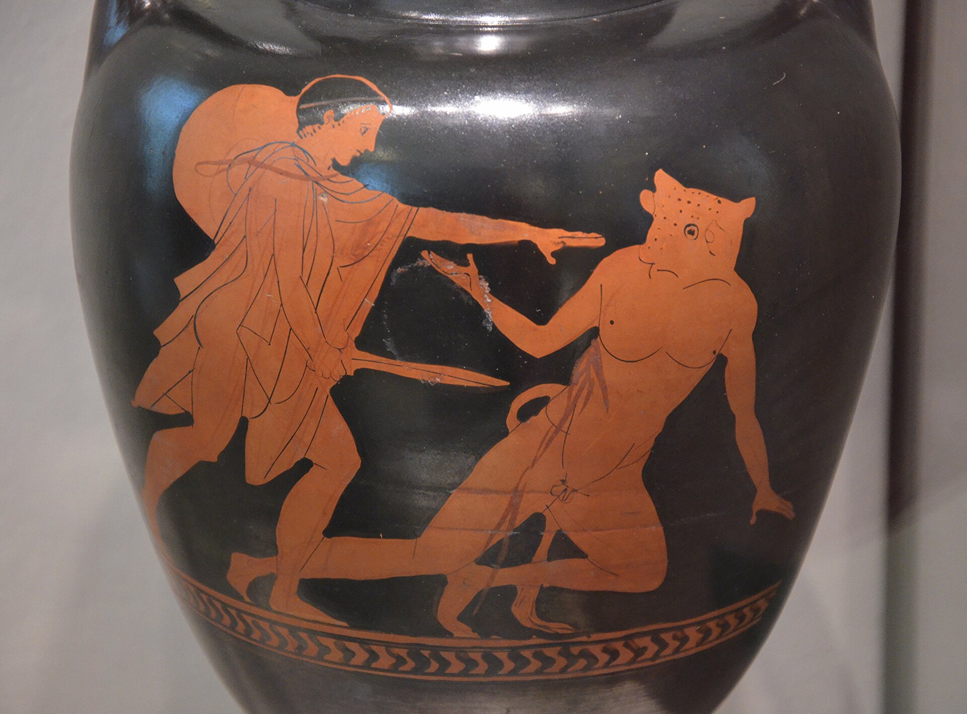 Iustracja przedstawia malowidło zdobiące wazę „Walka Tezeusza z Minotaurem”. Ukazuje ono Tezeusza zadającego Minotaurowi śmiertelny cios. Minotaur brodząc krwią, pada na ziemię. 