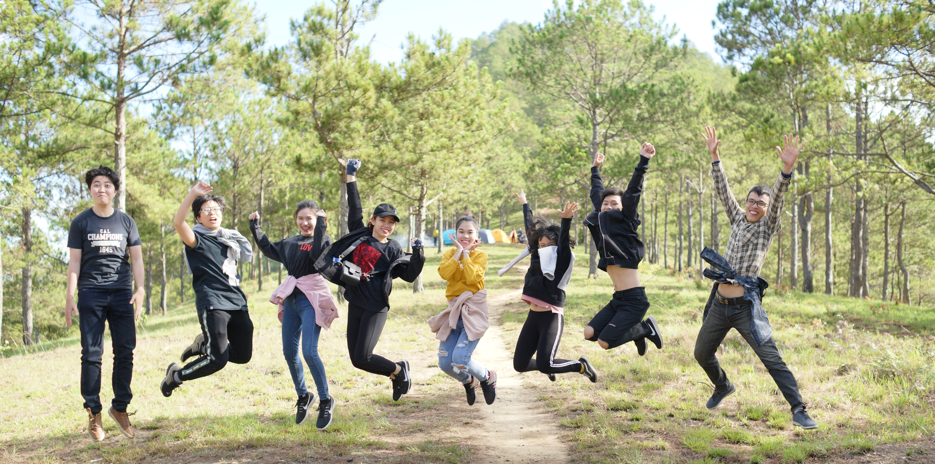 Zdjęcie przedstawia grupę ośmiu nastolatków na wycieczce w lesie. Zdjęcie zostało wykonane w momencie, gdy młodzież podskoczyła. Nie dotykają ziemi.