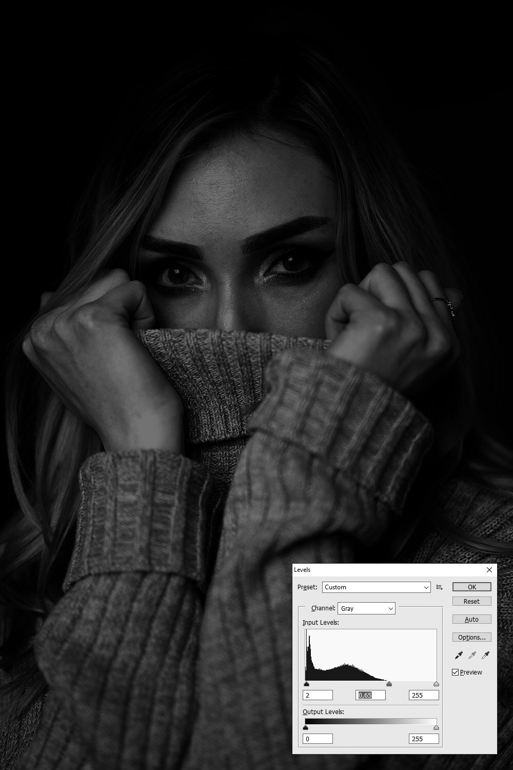 Zrzut ekranu ukazuje zdjęcie kobiety z widoczną zmianą koloru na bardzo ciemny.  Na dole znajduje się okno dialogowe: levels.  Znajdują się w nim: Pole: Preset z wybrana opcją: Custom.  Poniżej znajduje się pole Channel z wybraną opcją: RGB.  Następnie widoczny jest podgląd: input levels przy którym możemy manewrować strzałkami lub polami, w które można wprowadzić wartości.  W polach tych wpisano: 2, 0,65 oraz 255   Następnie widoczny jest suwak Output levels, do którego także można wpisać wartości w dwa pola znajdujące się poniżej.  W polach tych wpisane są wartości: 0 oraz 255.  W oknie po prawej stronie zaznaczona jest opcja: Preview.  Okno to zawiera takie przyciski jak: ok, reset, auto, options.