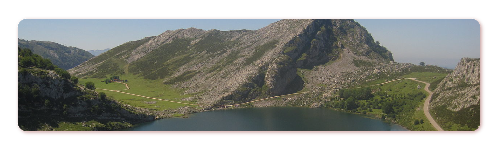Zdjęcie przedstawia jezioro Covadonga w górach Picos de Europa. Jezioro otoczone przez szczyty górskie z widocznymi drogami.