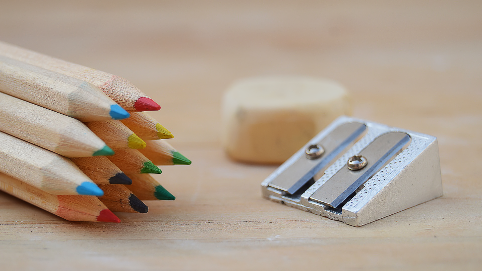 Zdjęcie przedstawia metalową temperówkę. Obok leżą zatemperowane kredki ołówkowe.