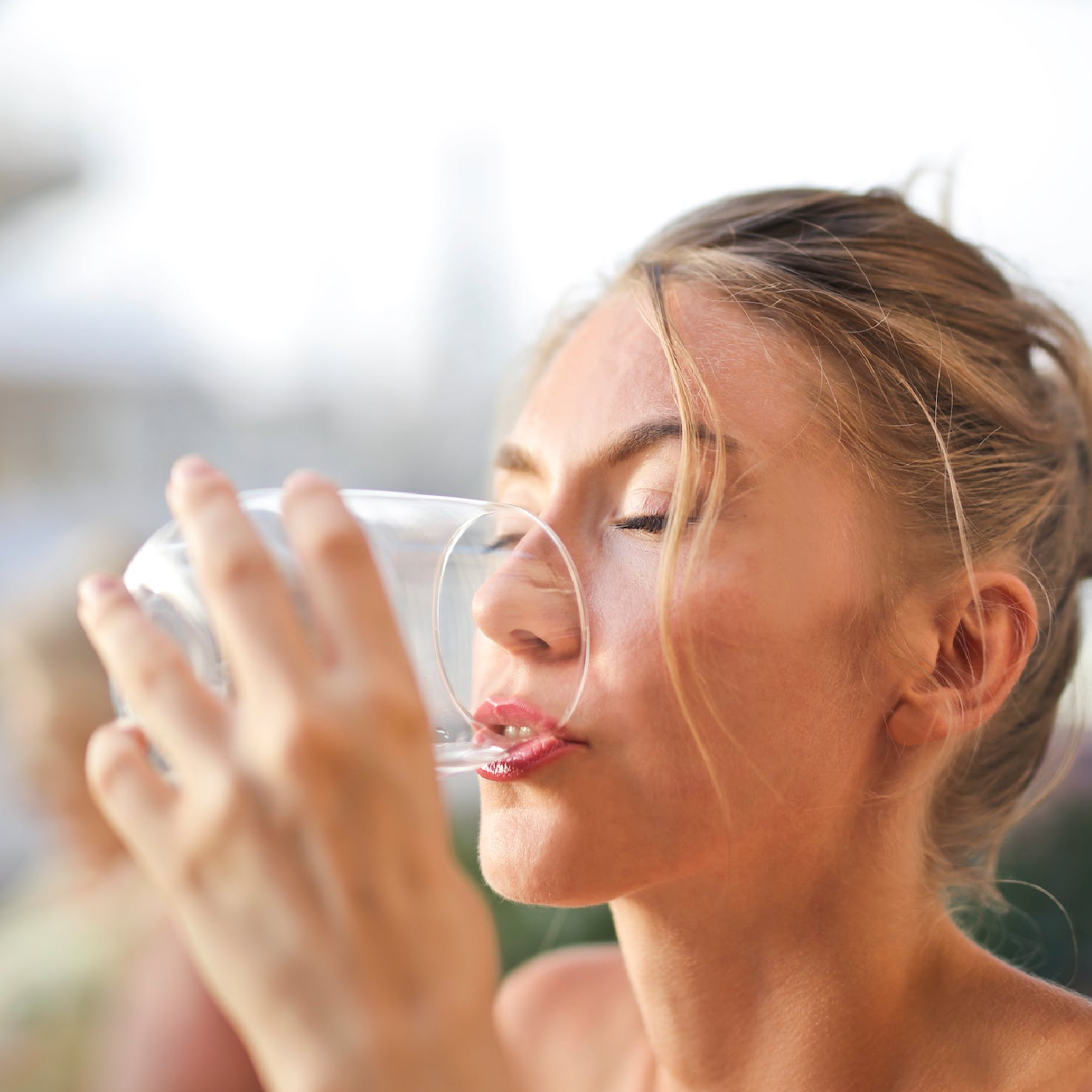 Zdjęcie przedstawia blondwłosą kobietę, pijącą wodę ze szklanki.