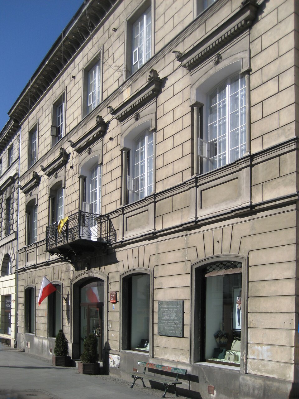 Na zdjęciu przedstawiono klasycystyczną, trzypiętrową kamienicę miejską. Fasada budynku jest symetryczna, z prostokątnymi oknami ozdobionymi profilowanymi obramieniami. Nad wejściem znajduje się balkon z kutą balustradą. Przy drzwiach wisi flaga Polski, a obok umieszczono tablicę pamiątkową. Na chodniku stoją dwie donice oraz ławka.