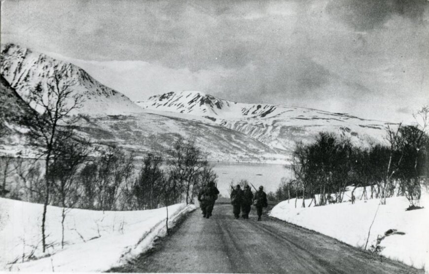 Zdjęcie przedstawia kliku żołnierzy idących drogą wśród ośnieżonych pół i gór.