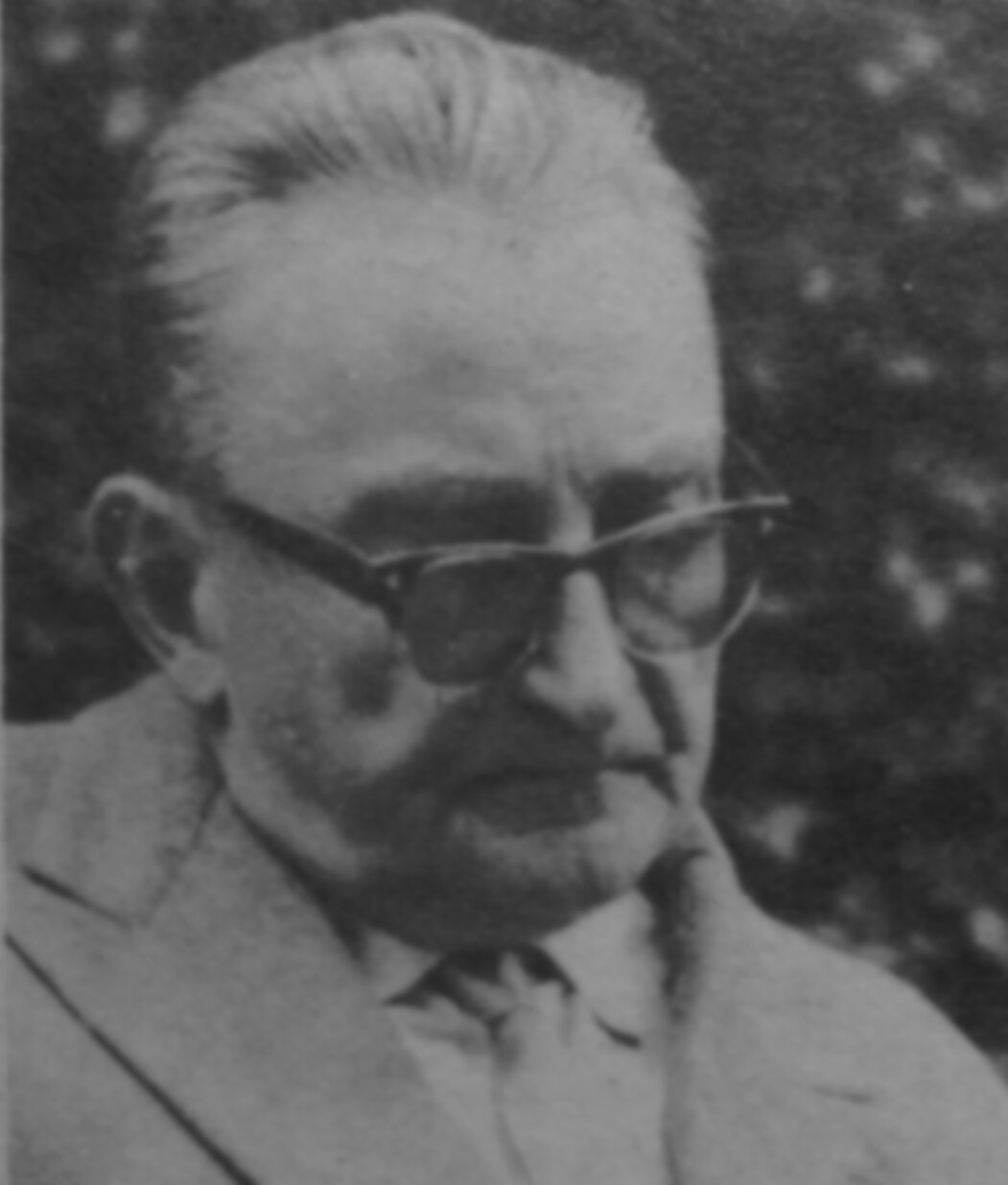 Kliknij, aby powiększyć Czarno‑biała fotografia przedstawia popiersie poety Jana Sztaudyngera. Starszy mężczyzna nosi okulary, włosy ma zaczesane do góry, jego głowa zwrócona jest lekko w prawo, wzrok wpatrzony w dół. Nosi marynarkę, koszulę, na szyi ma zawiązany krawat. Tło jest ciemne.