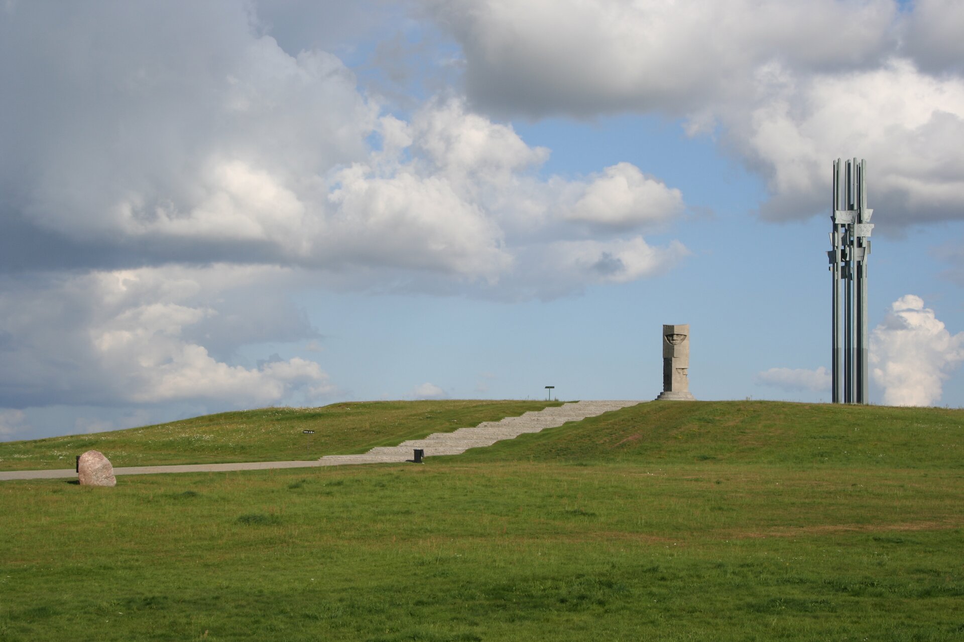 Na zdjęciu wzgórze, na szczycie kamienny obelisk, do którego prowadzą kamienne schody, obok metalowa konstrukcja składająca się z kilku wysokich masztów.