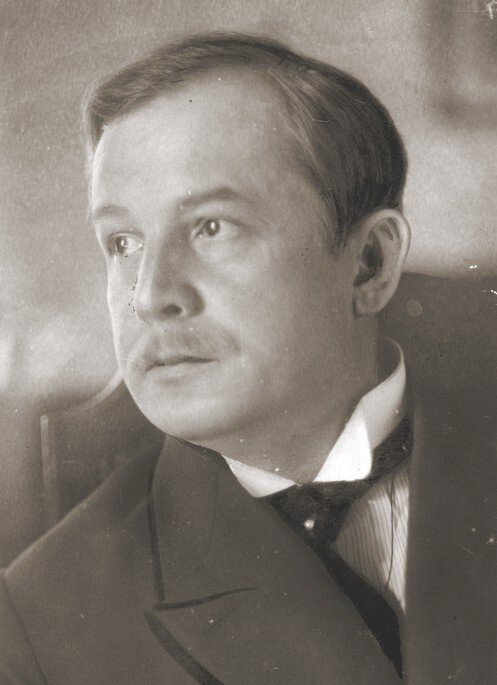 Zdjęcie przedstawia mężczyznę z wąsem, włosami zaczesanymi na bok. Ubrany w garnitur, pod szyją krawat. 